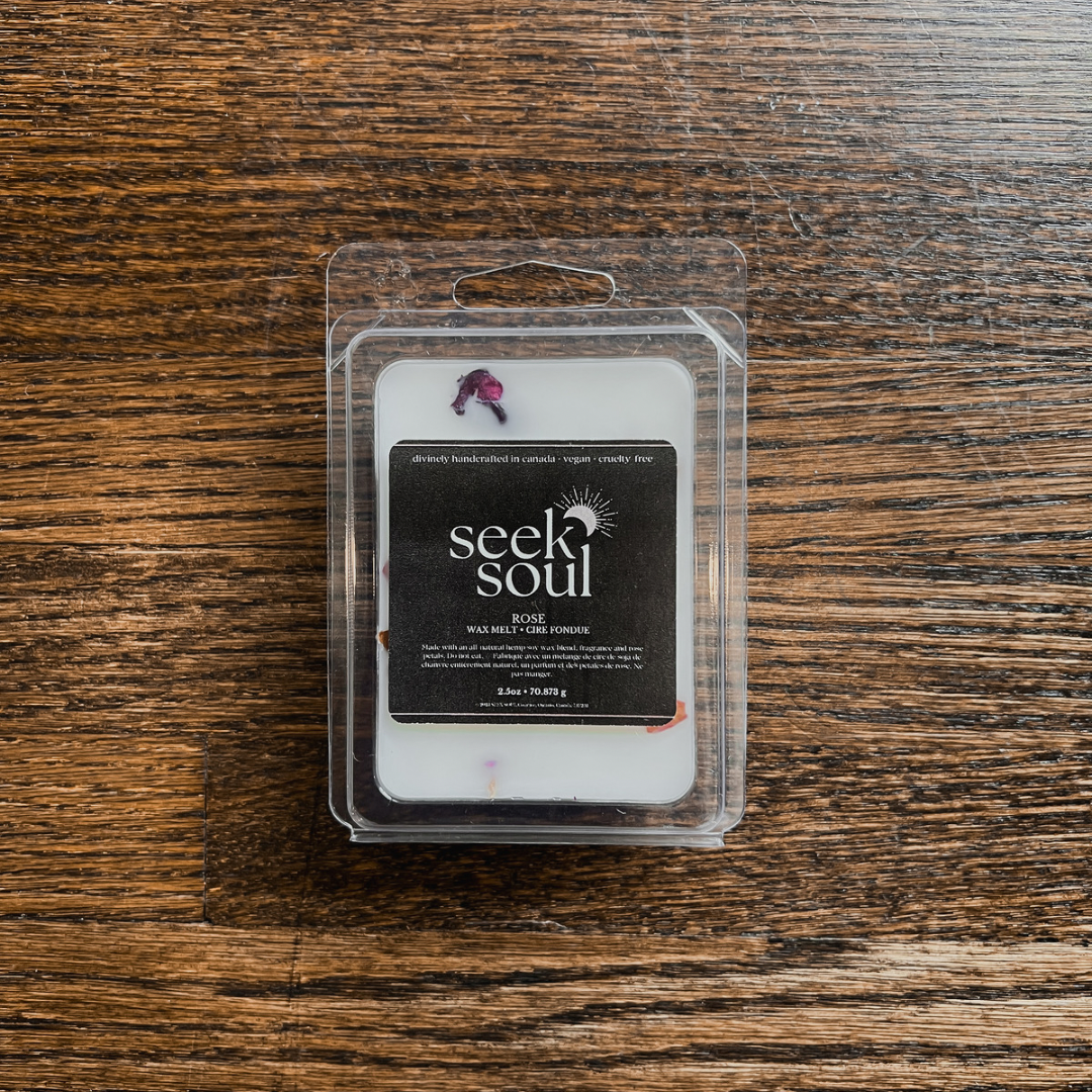 Photo of our Rose Wax Melts. Melts are white in colour with pink rose petals scattered throughout. There are 6 large cubes. Packaging is clear, recyclable and approximately 4” long. Box has a black label on the front with the SEEK SOUL logo on it.