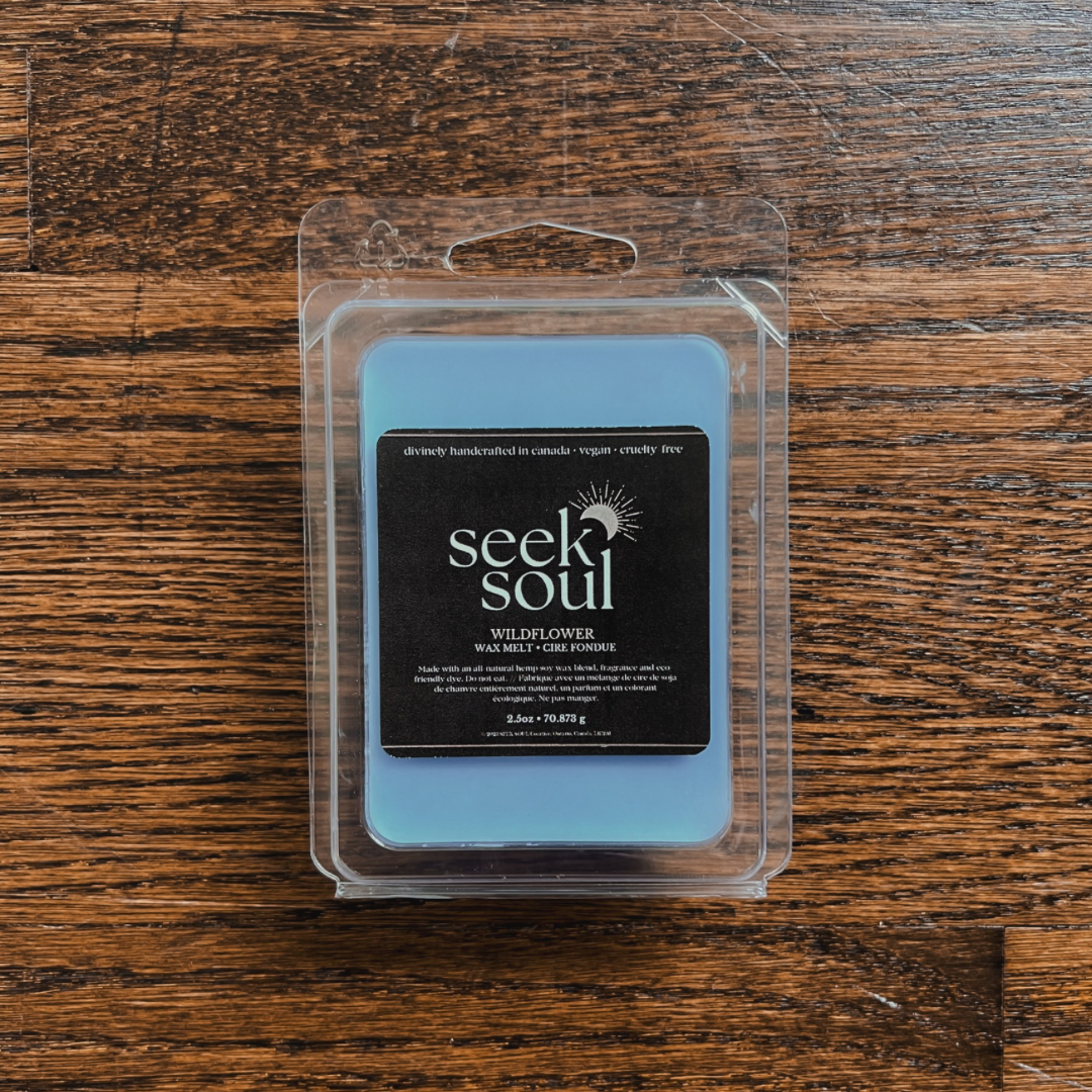 Photo of our Wildflower Wax Melts. Melts are blue and there are 6 large cubes. Packaging is clear, recyclable and approximately 4” long. Box has a black label on the front with the SEEK SOUL logo on it.
