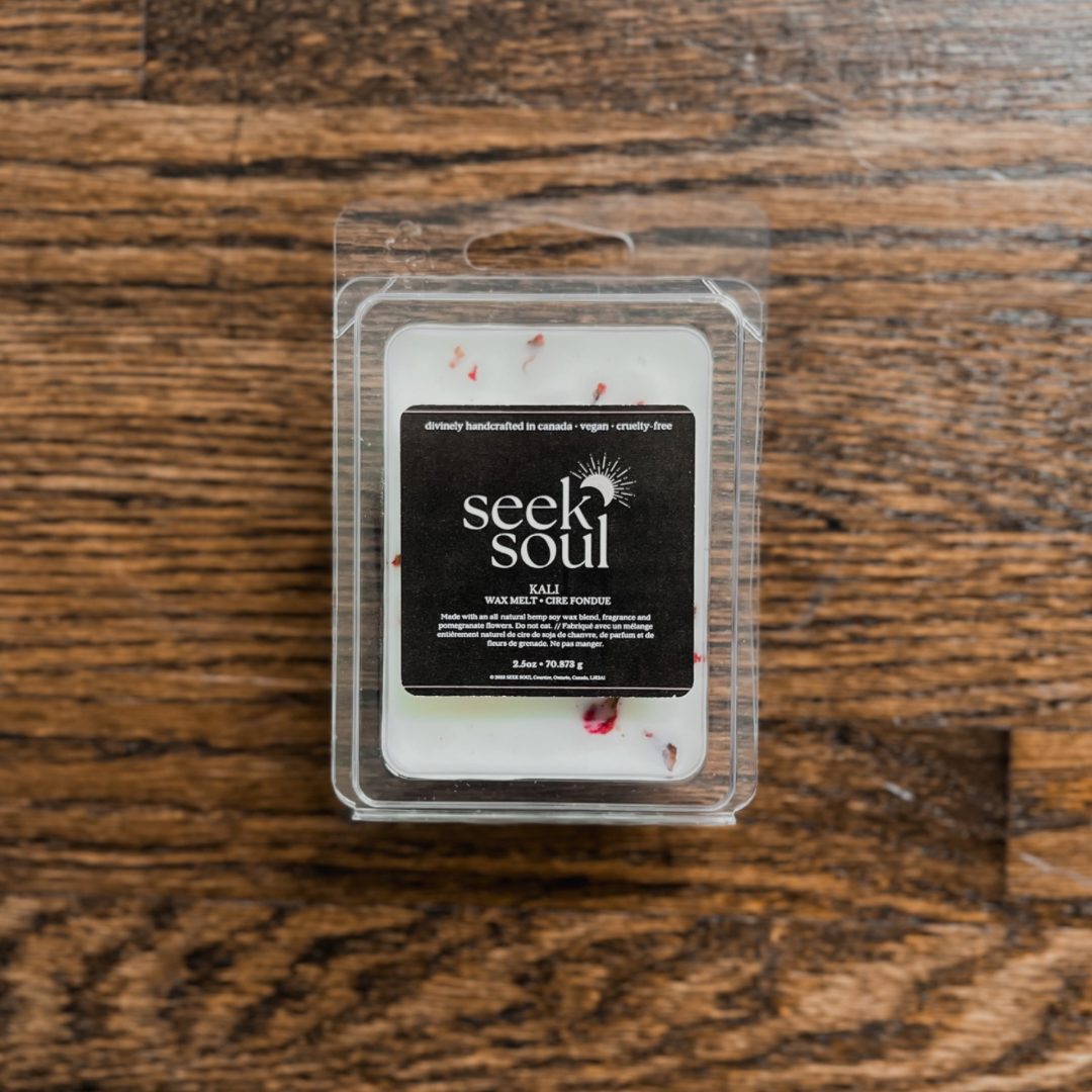 Photo of our Kali Wax Melts. Melts are off-white in colour with red pomegranate flowers scattered throughout. There are 6 large cubes. Packaging is clear, recyclable and approximately 4” long. Box has a black label on the front with the SEEK SOUL logo on it.