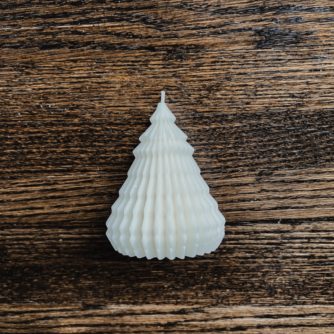 Photo of our Frankincense Tree Candle. The wax is off-white and the candle has a cotton wick. The candle has no jar, it is free-standing and is defined by jagged, vertical lines running up and down the candle to make it look like an evergreen tree. It just under 4” tall.