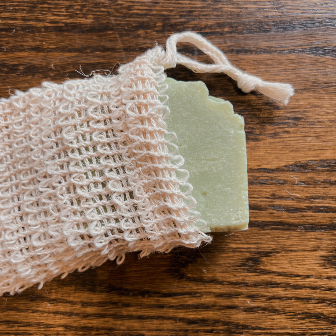 A photo of our sisal soap bag. The material is made of beige, natural fibres woven together to help gently exfoliate the skin. There is a drawstring on top. In this photo, we have our green Australian Tea Tree soap in the bag to demonstrate.