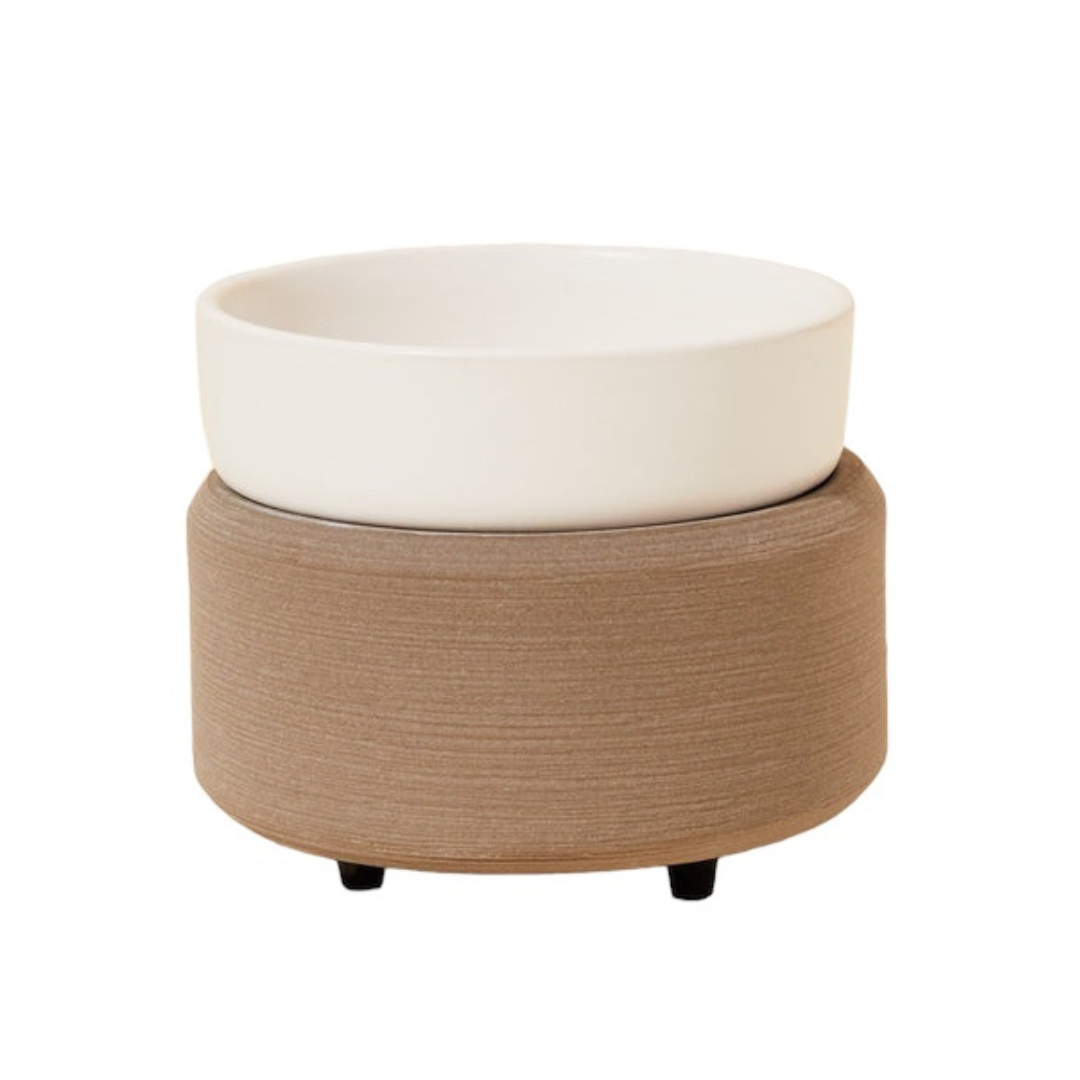 Photo of our Stone Wax Warmer. It is circular in shape with a removable round dish sitting on top. It has tiny black feet on the bottom and is  grey in colour with a white dish. 