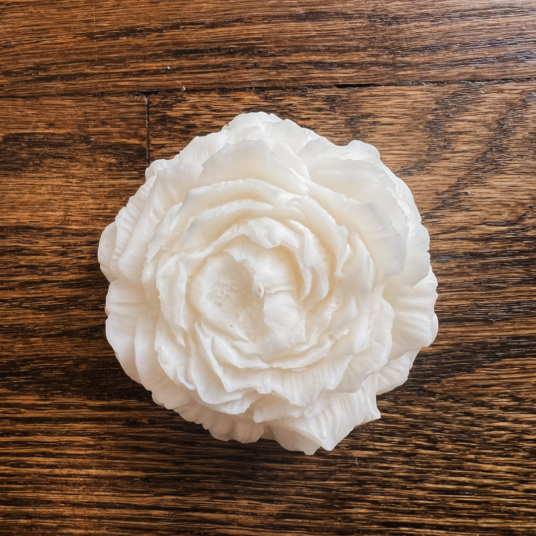 Photo of our Rose Peony Candle. The wax is white and the candle has a cotton wick. The candle has no jar, it is free-standing and has detailed and realistic-looking petals. It is around 3” wide.